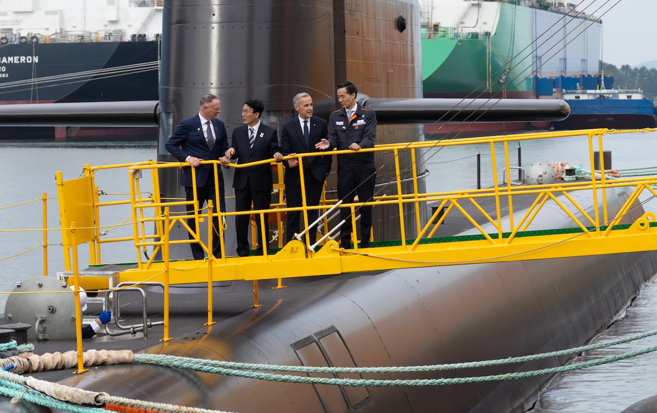 Four men are shown standing on a yellow ramp to a submarine.