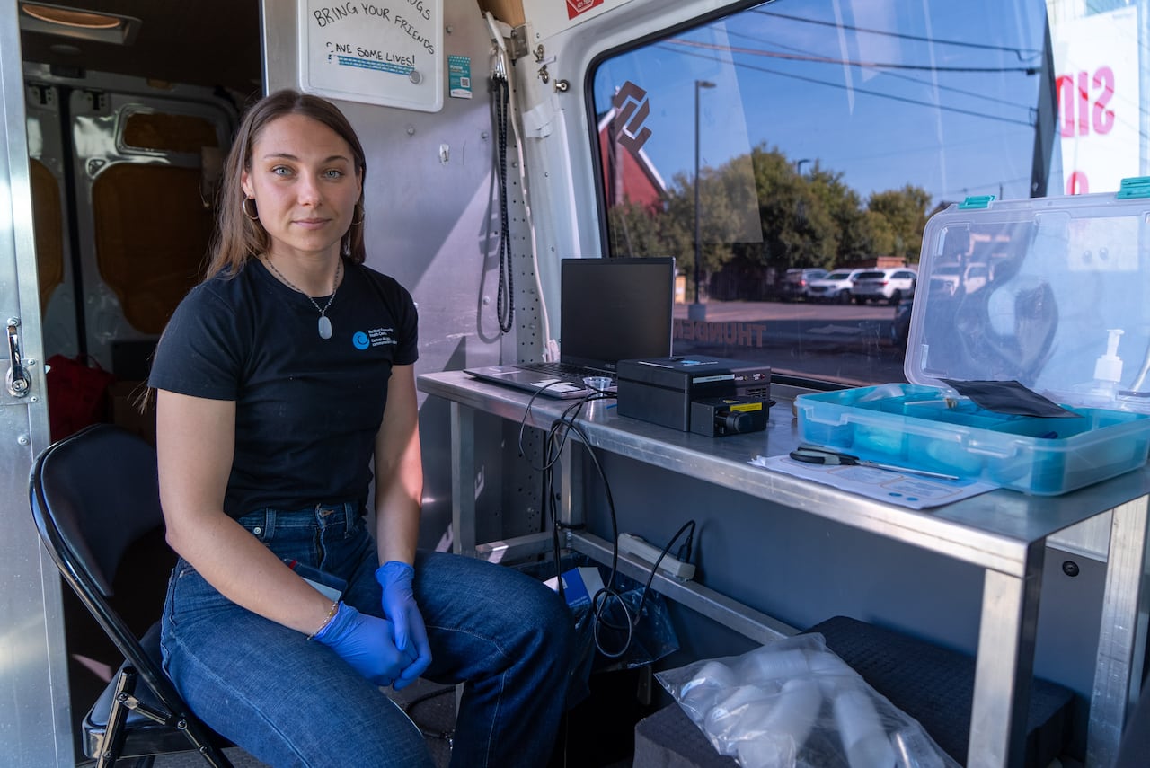A person wearing medical gloves is seen sitting inside a medical van.