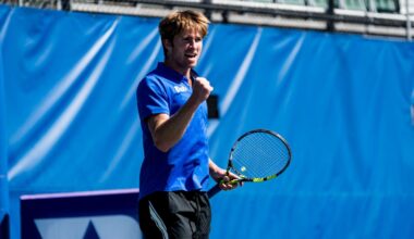 Theo Winegar fist pumps for a posed photo wearing a Duke blue shirt in front of a white backdrop.
