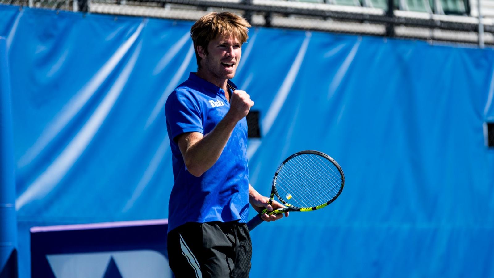 Theo Winegar fist pumps for a posed photo wearing a Duke blue shirt in front of a white backdrop.