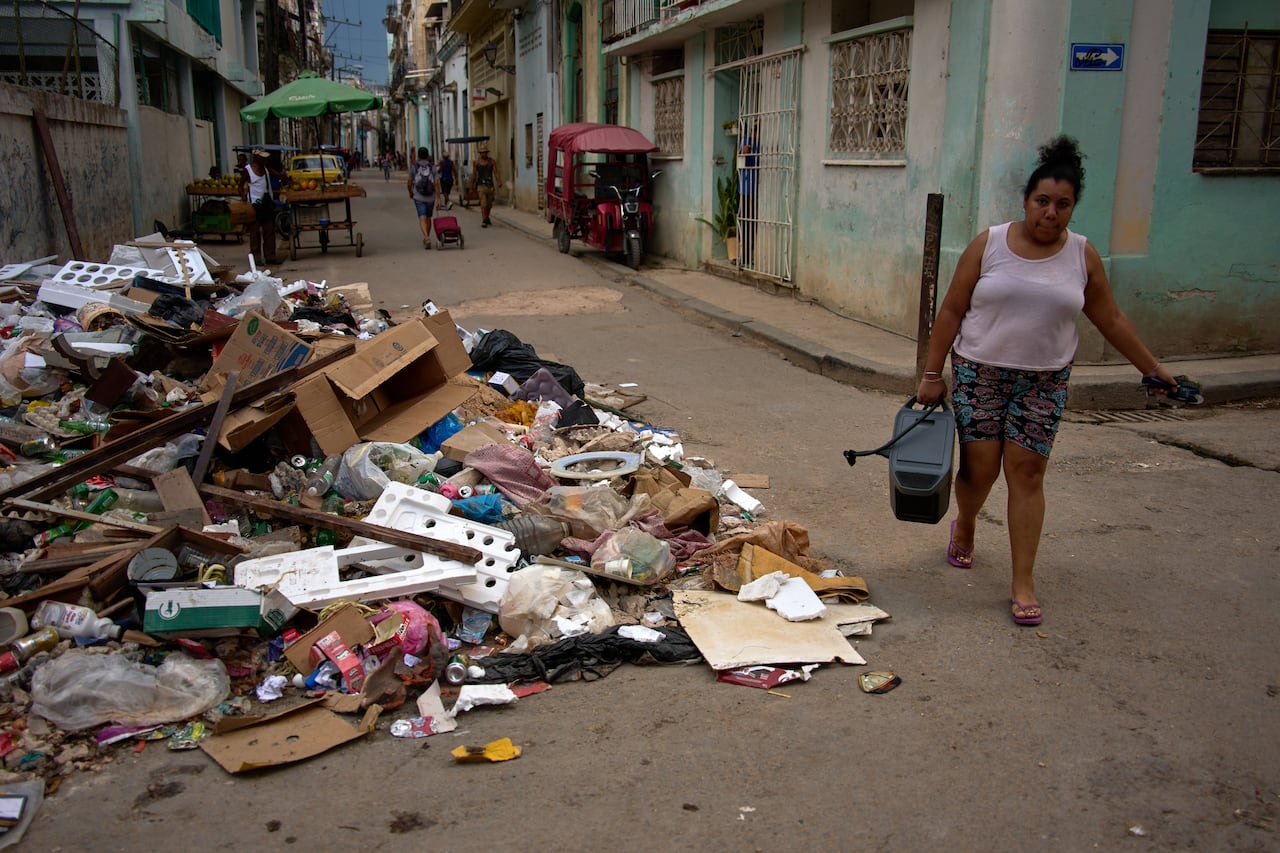 A woman carries a portable power charger, while walking past a pile of trash in Havana.