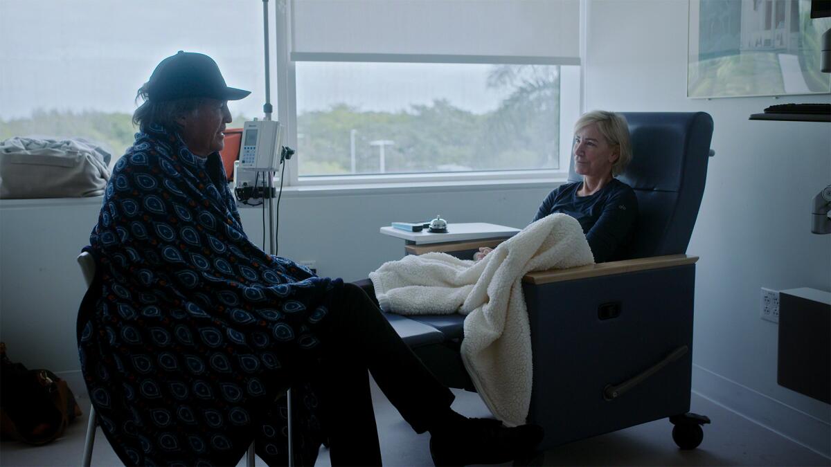 A man and a woman sit across from one another in a hospital room.
