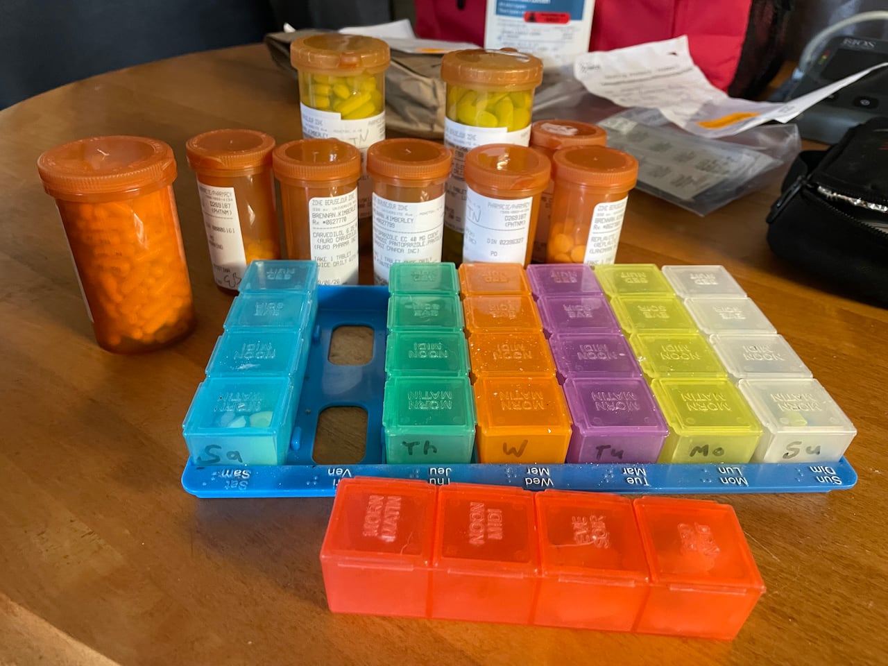 Several pill bottles and a weekly medication sorter sitting on a kitchen table.