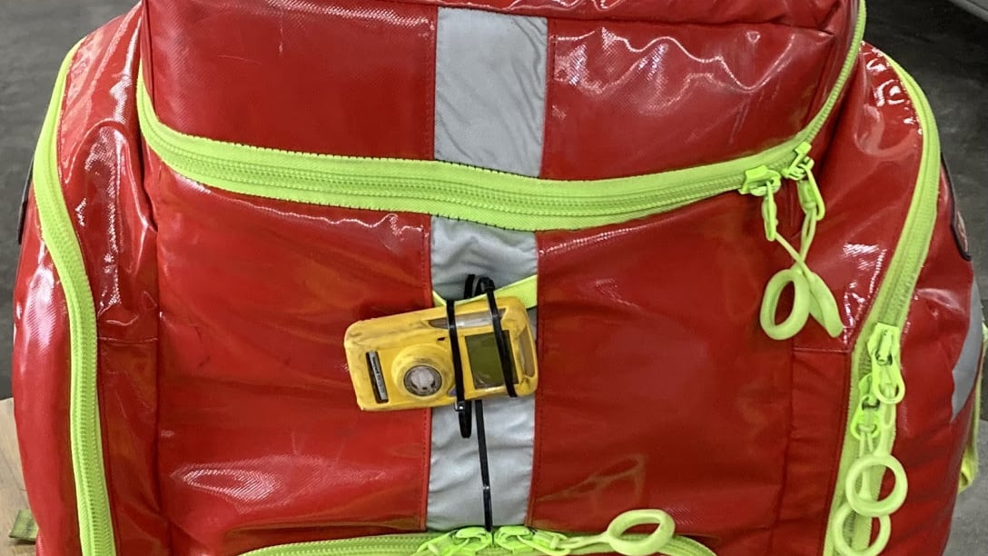 A shiny red backpack with a reflective white stripe down the middle and bright yellow-green zippers.