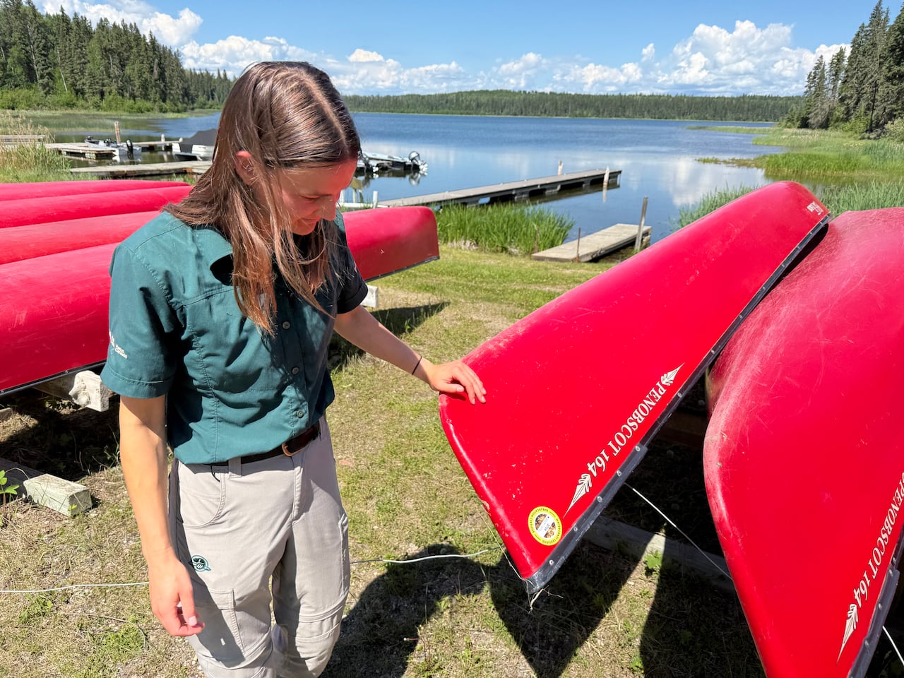 A young woman with long dark brown hair looks at red canoe to check for an aquatic invasive species compliance sticker.