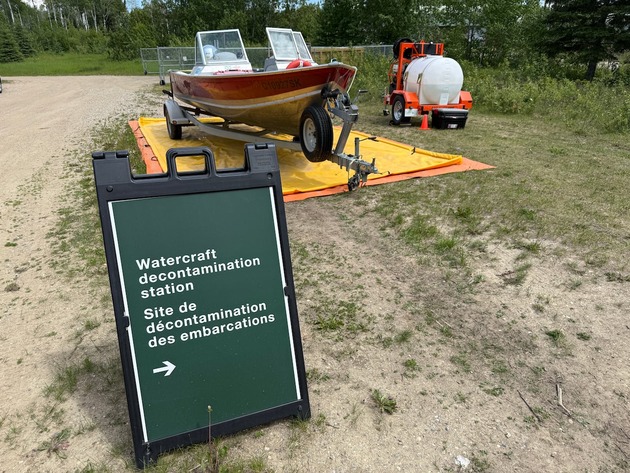 A folding sign board saying watercraft decontamination station sits outside near a boat.