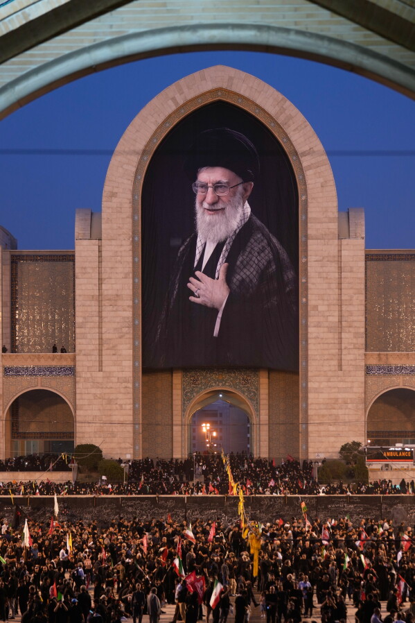 Mourners gather beneath a portrait of the late Iranian Supreme Leader Ayatollah Ali Khamenei during the funeral ceremonies for Khamenei and members of his family at the Imam Khomeini Mosalla Grand Mosque in Tehran, Iran, Saturday, July 4, 2026. (AP Photo/Altaf Qadri)