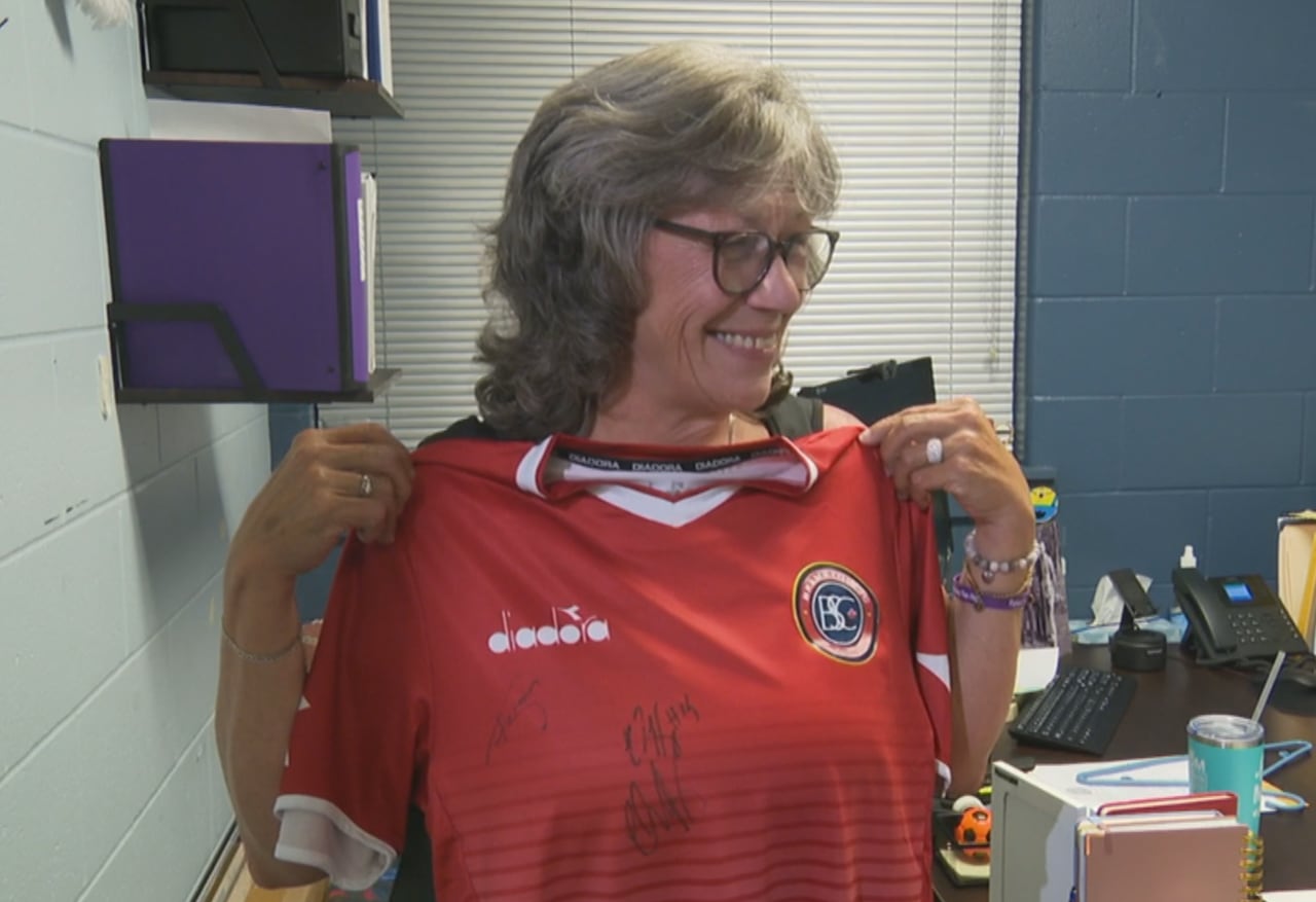 a woman with grey hair is holding a signed red jersey with a smile