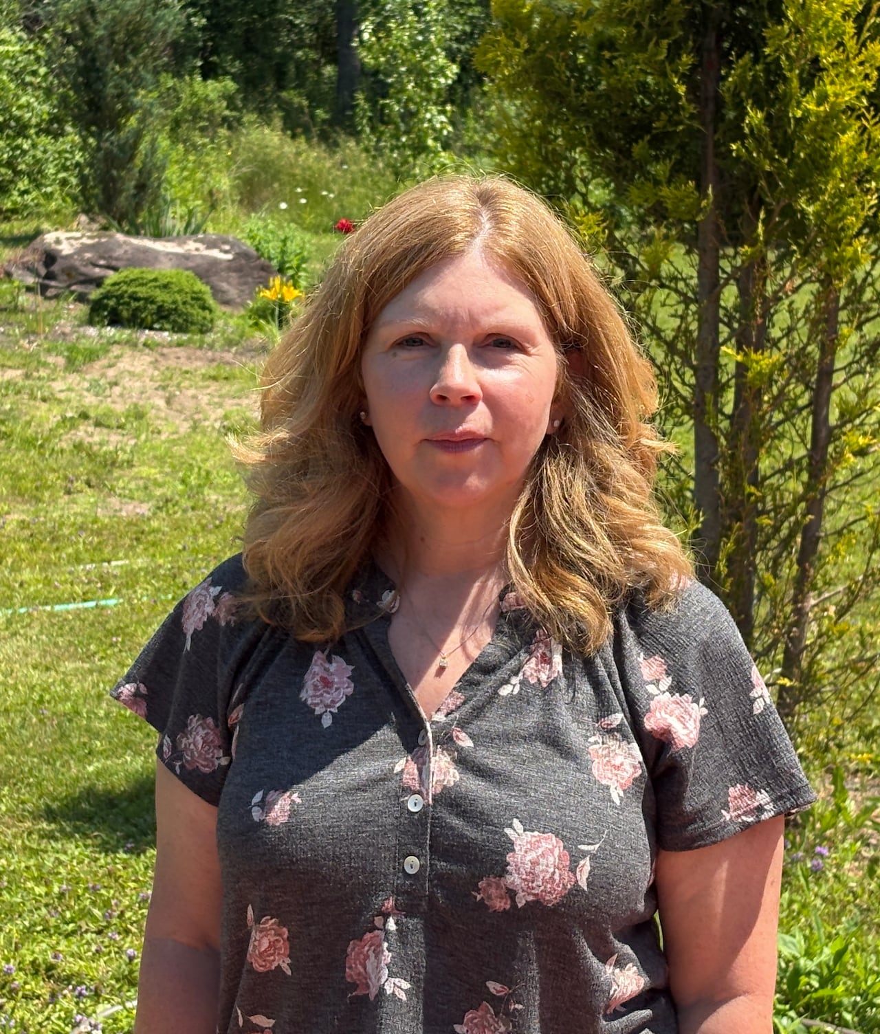 Woman, looking at camera with a neutral expression, on a sunny day.