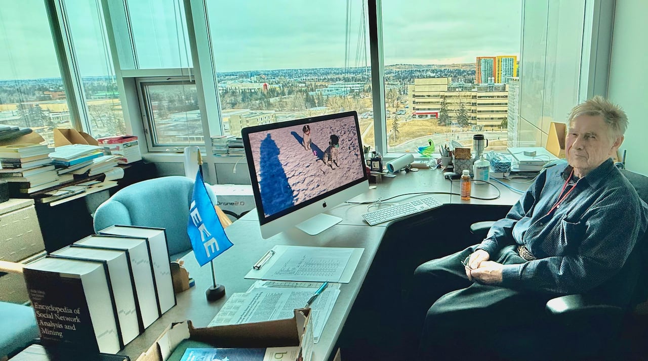 A man sits at a desk with a view of the university campus.
