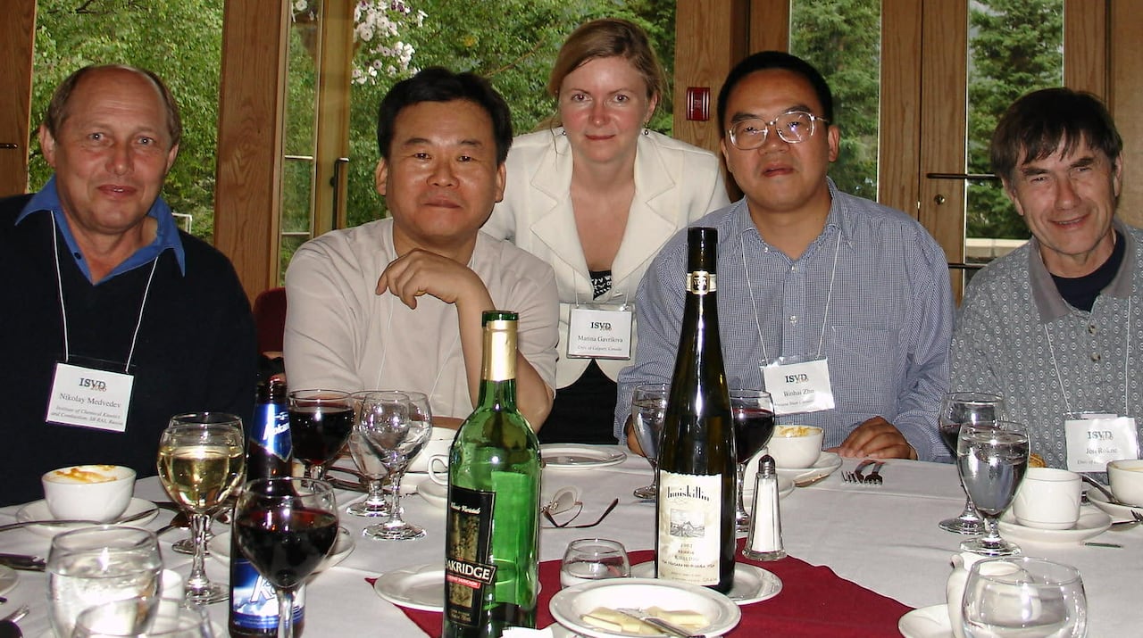 Five people sit around a dinner table and smile at the camera.