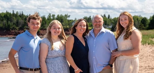 Five smiling people with their arms around each other pose on a beach.