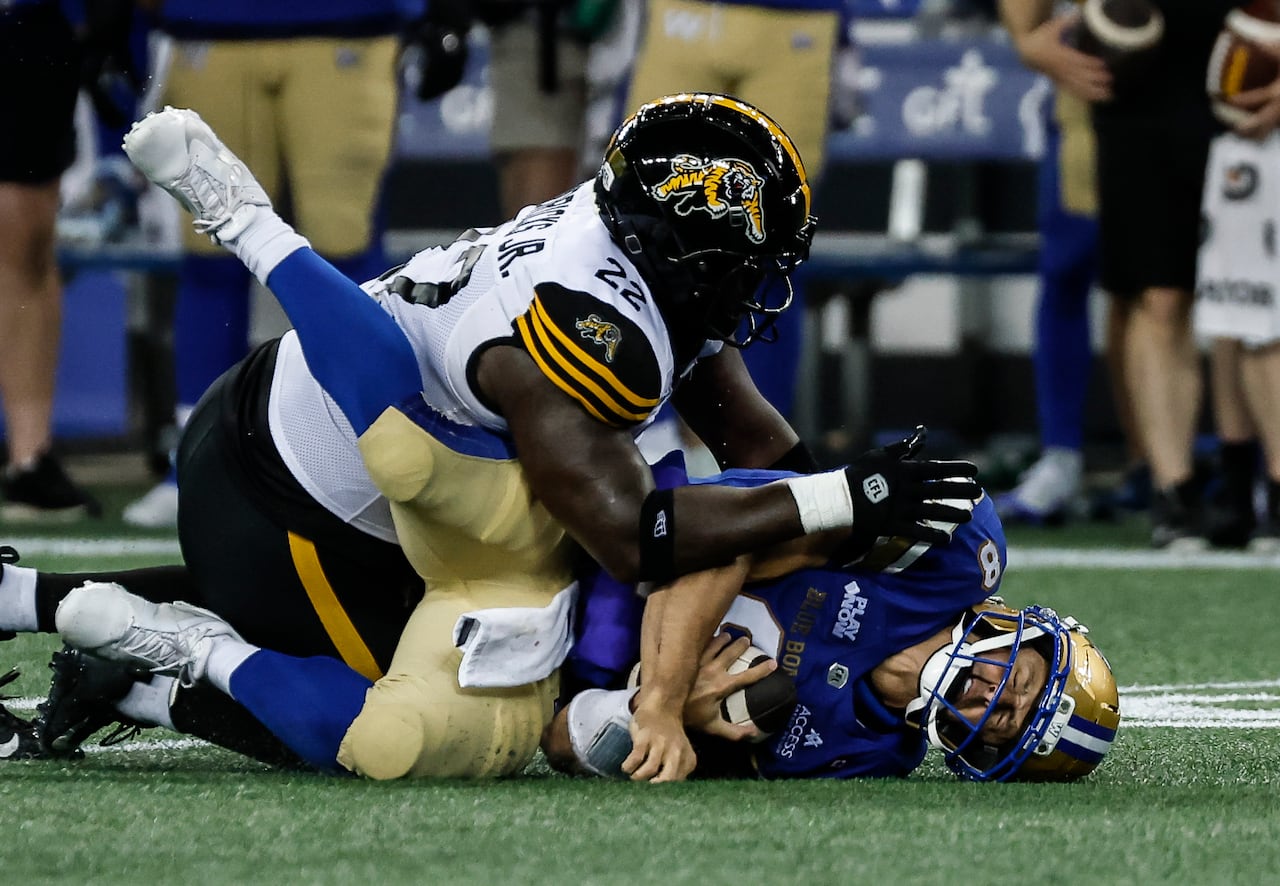Zach Collaros grimaces while lying on the field, with a Hamilton Tiger-Cat opponent on top of him.