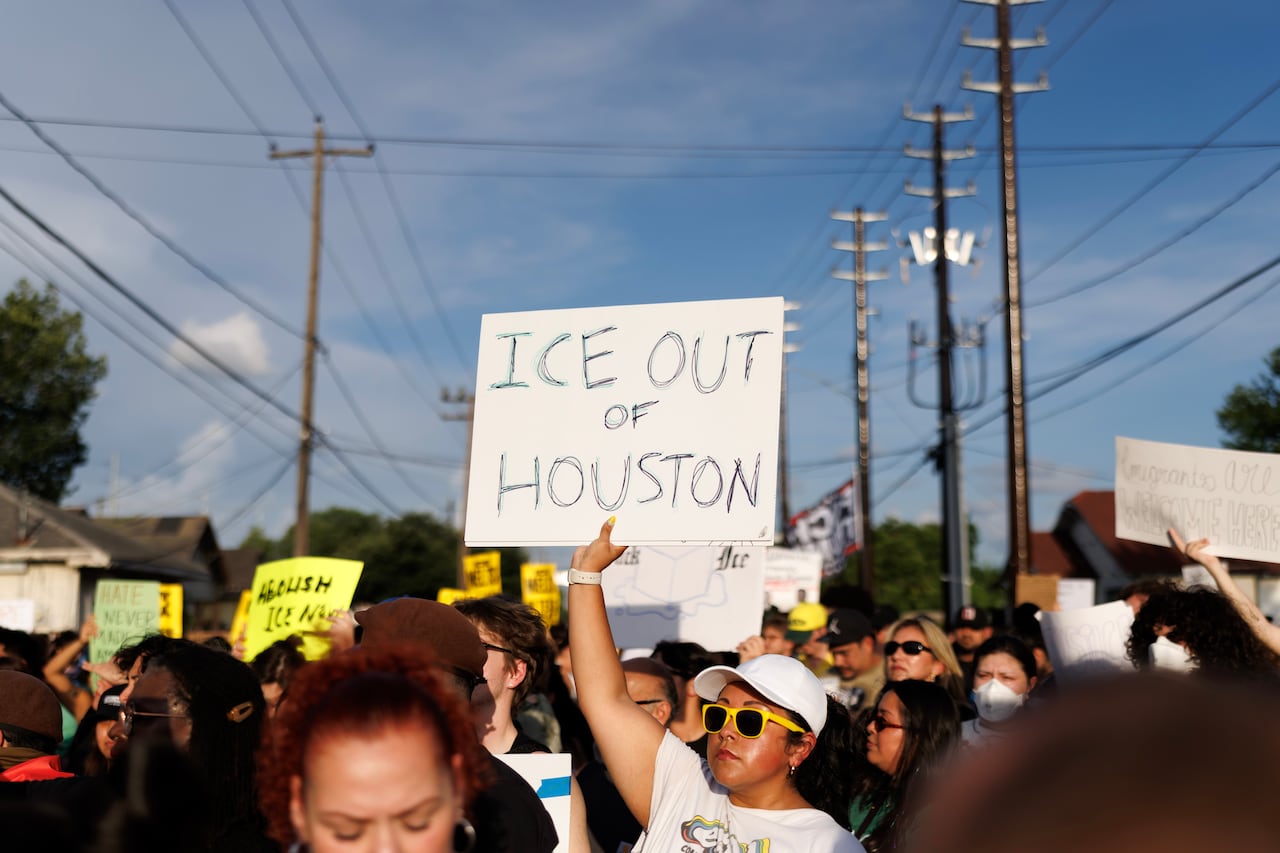People gather, some holding signs, including one that says Ice out of Houston