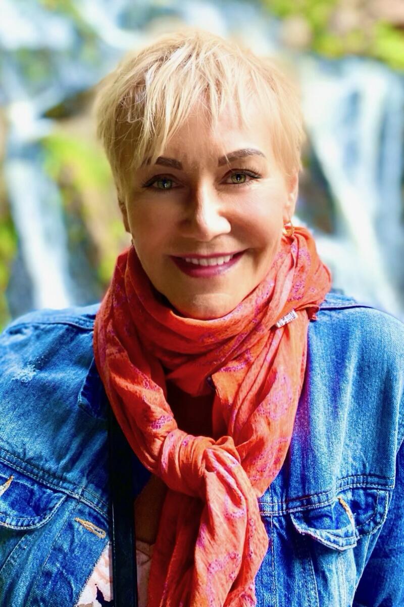 A blond woman in a denim jacket and pink scarf.