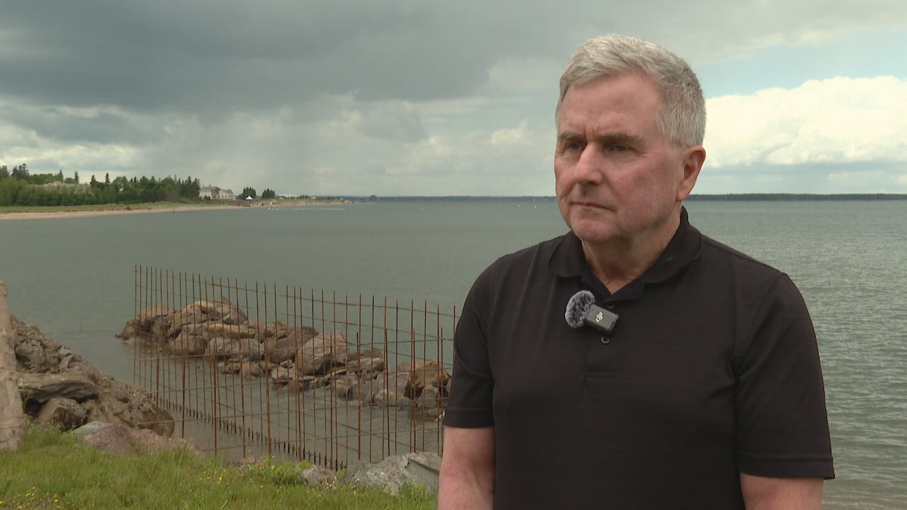 A man stands with sea wall under construction behind him.
