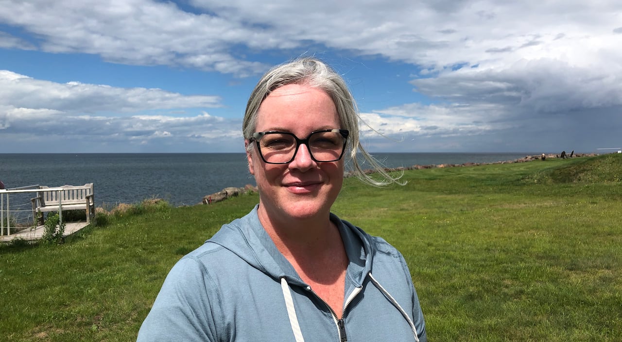 A woman standing on a grassy bank with rocks and water in distance.