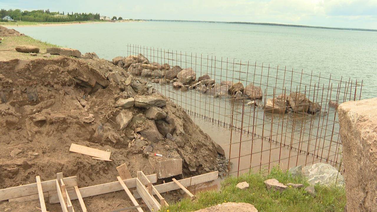 A sandy cliffside with wooden structure under construction around it, with several feet of water at base.