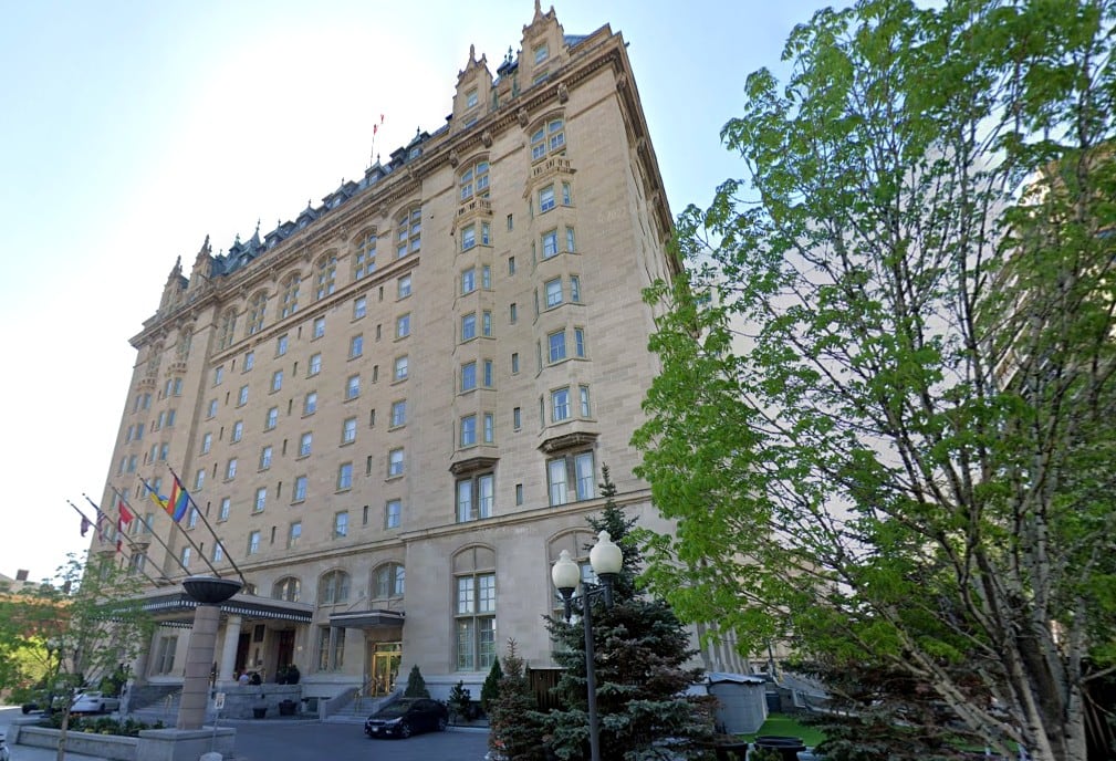 A tall, old stone hotel is seen from the street level looking up to the roof.