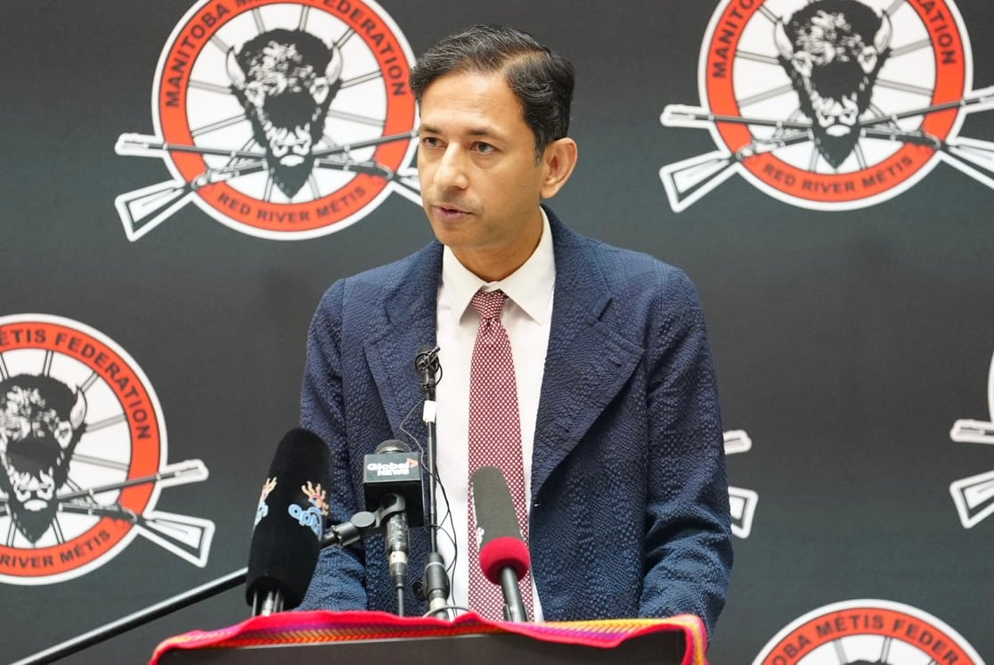 A man with short black hair, and wearing a suit, stands at a podium.