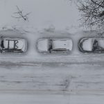 Cars parked on the side of the road, surrounded by snow.