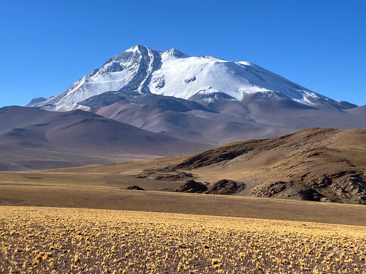 A snow-capped volcano stands high in a barren plane.