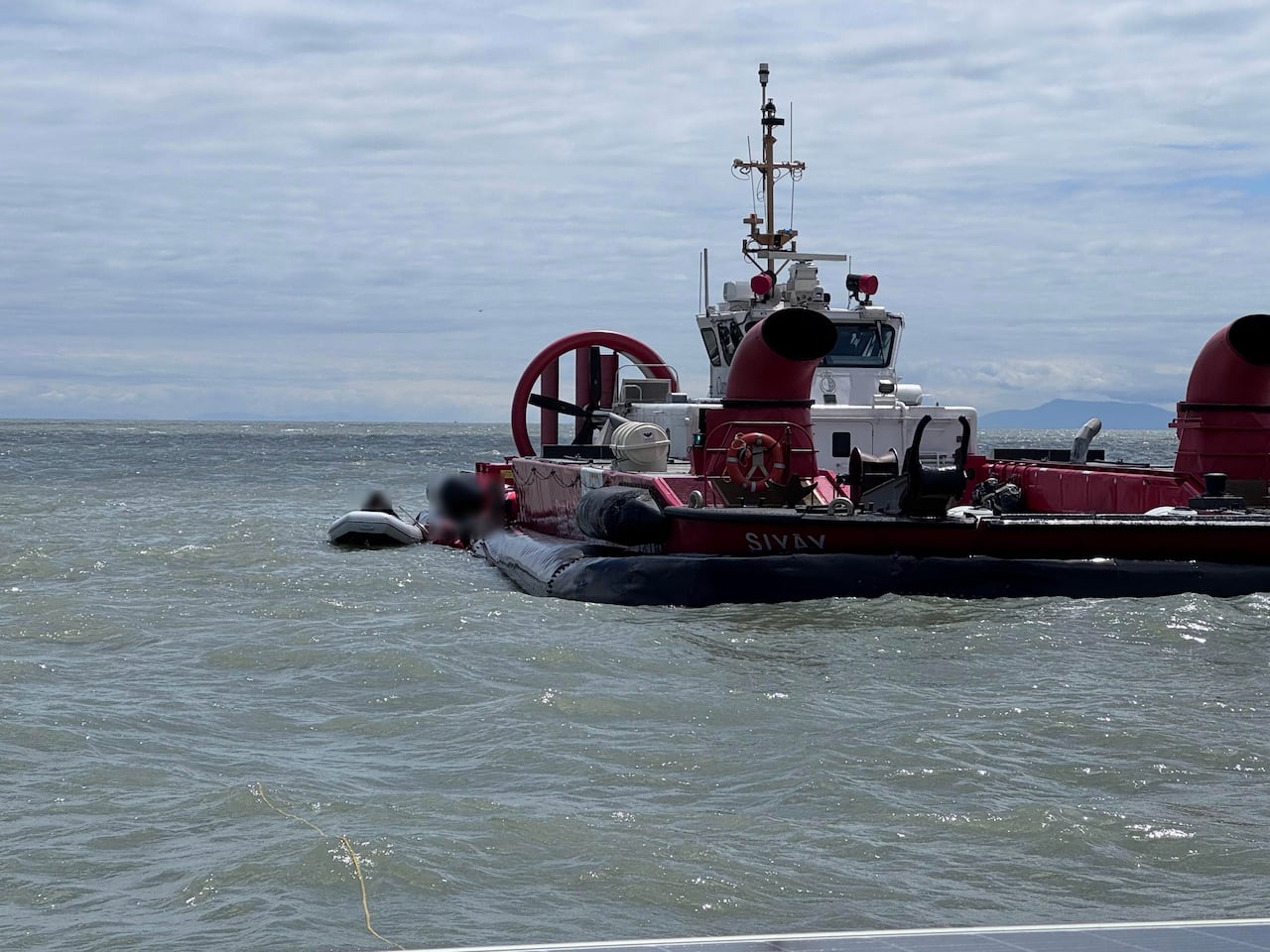 A red and white hovercraft next to a small grey dinghy in the ocean.