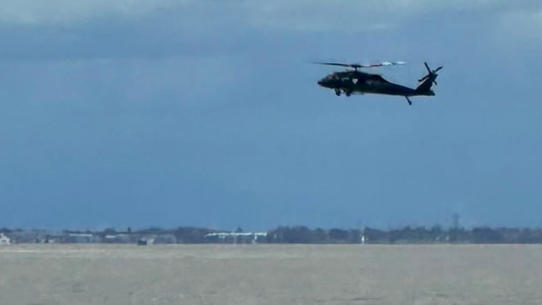 A black helicopter hovers over the ocean