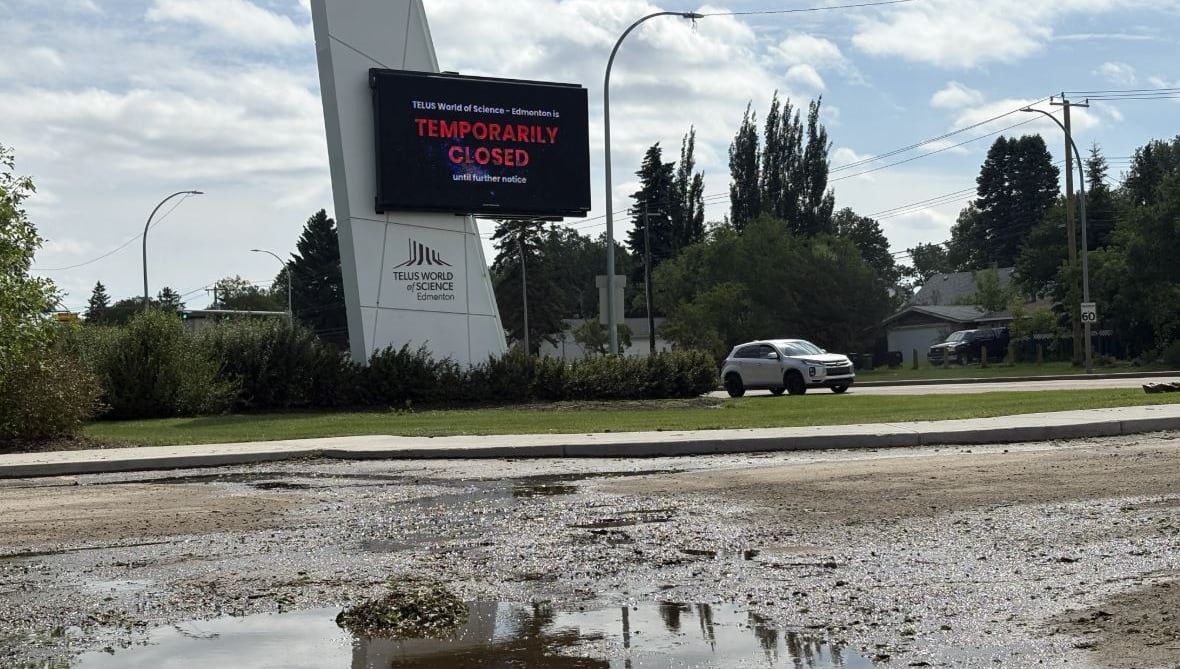 A puddle stands in a parking lot entryway, as an LED sign behind it advises of a building's temporary closure.