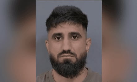 A mugshot of a man with a beard in front of grey background.