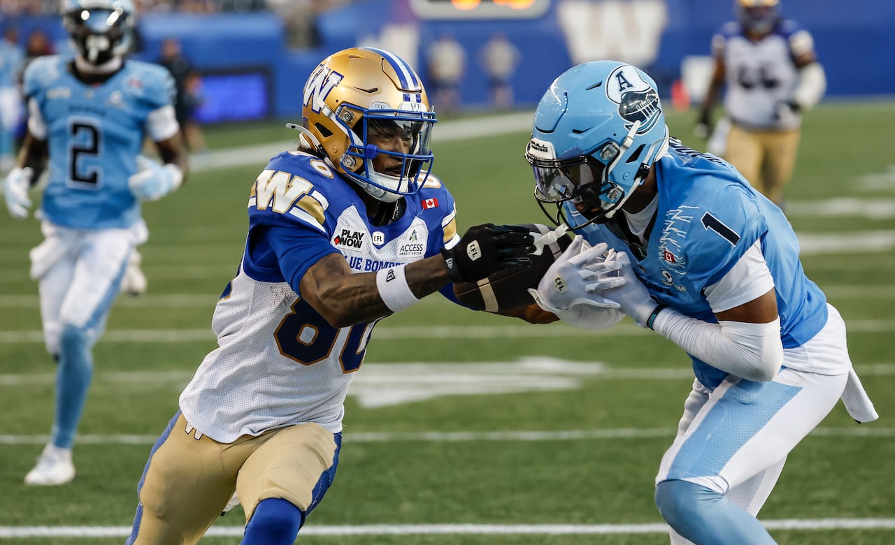 A football player in a gold, blue and white uniform holds a football as another player in light blue tries to intercept it