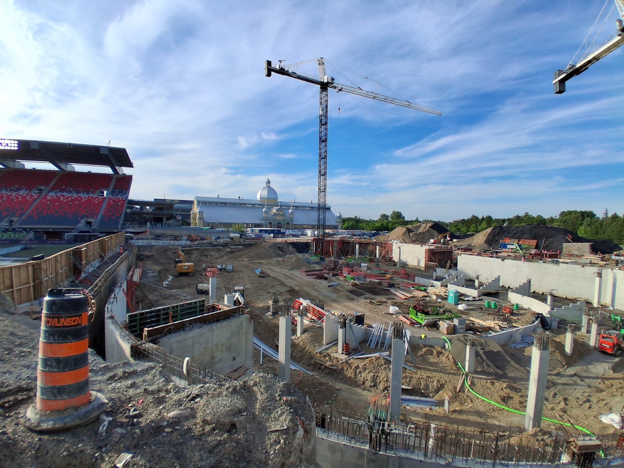 A large construction site in the foreground, with a crane, a historic building and a portion of a stadium's stands in the background.
