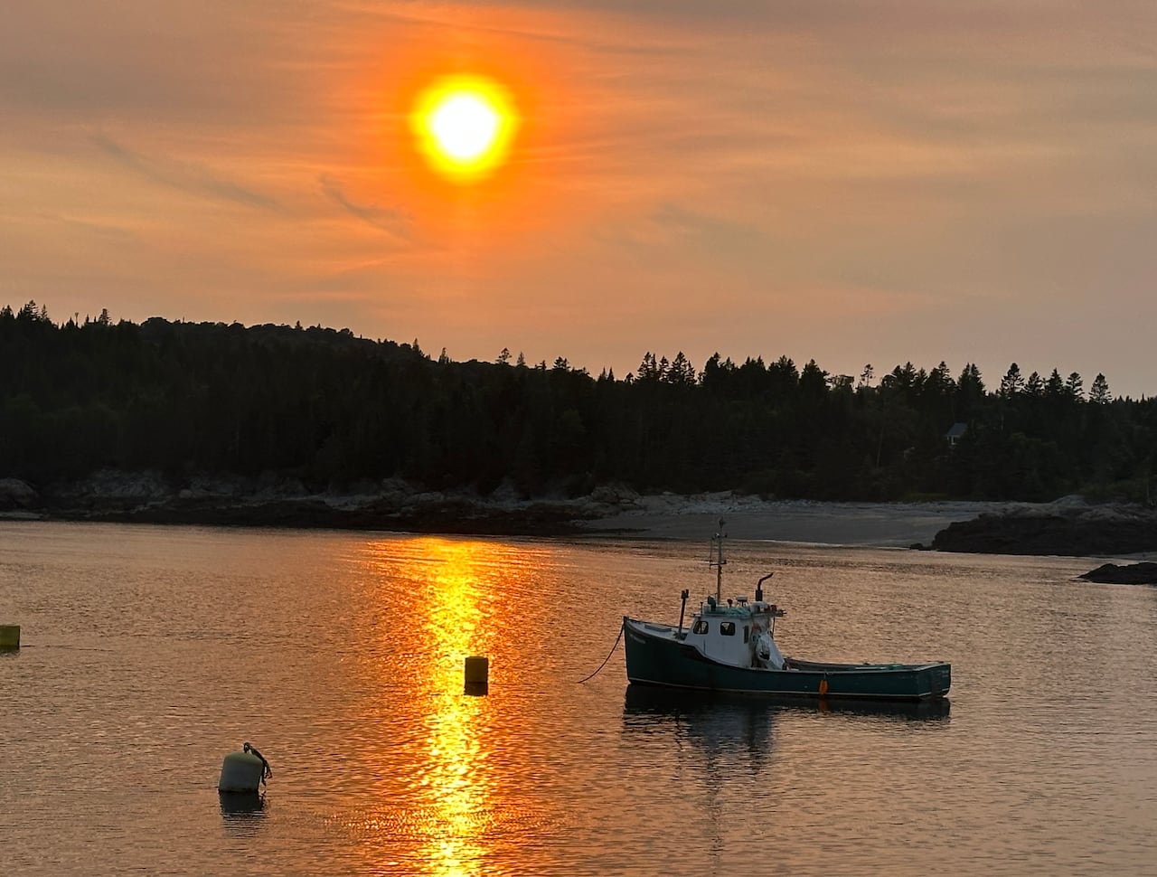A small fishing boat on the water during an orange sunset. The coast is in the background.