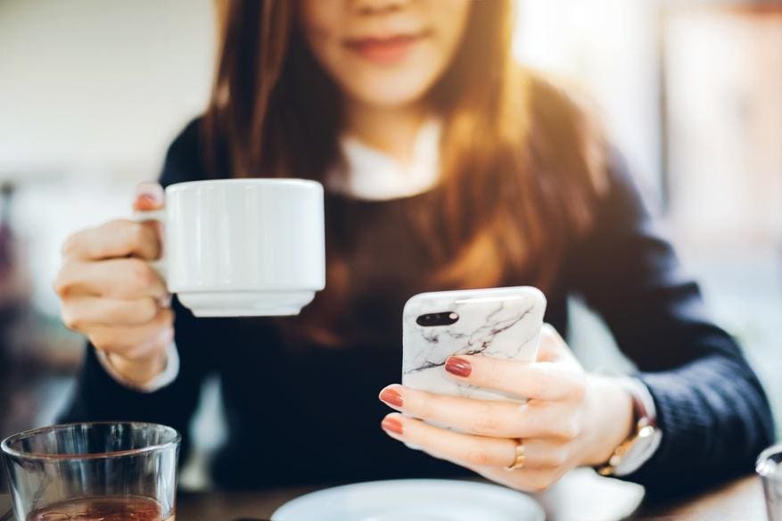 Close up of young woman having coffee with creatine and checking mobile phone before work