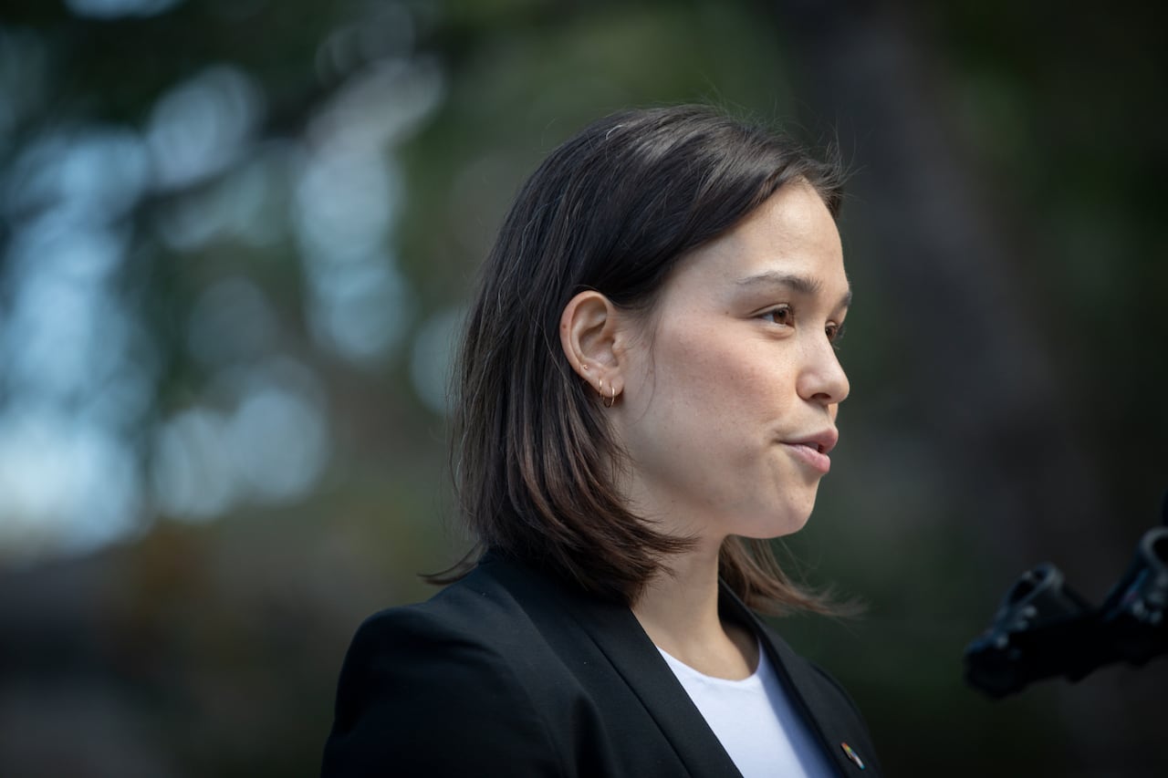 A woman with black hair is pictured in profile speaking to a mic.