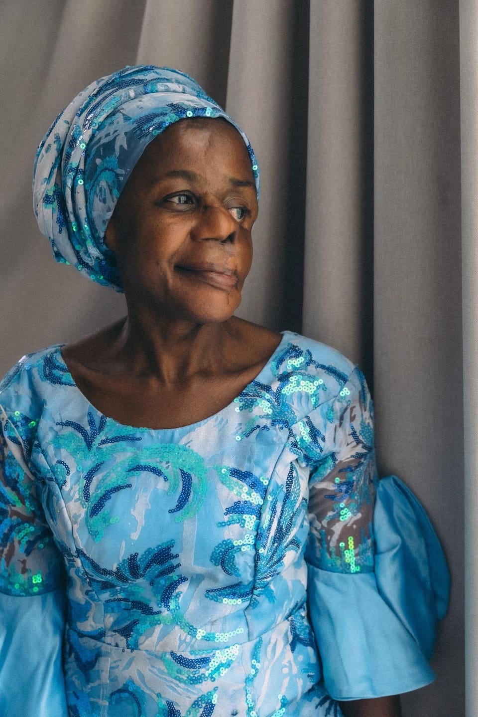 A woman in a blue headwrap and dress looks away from the camera