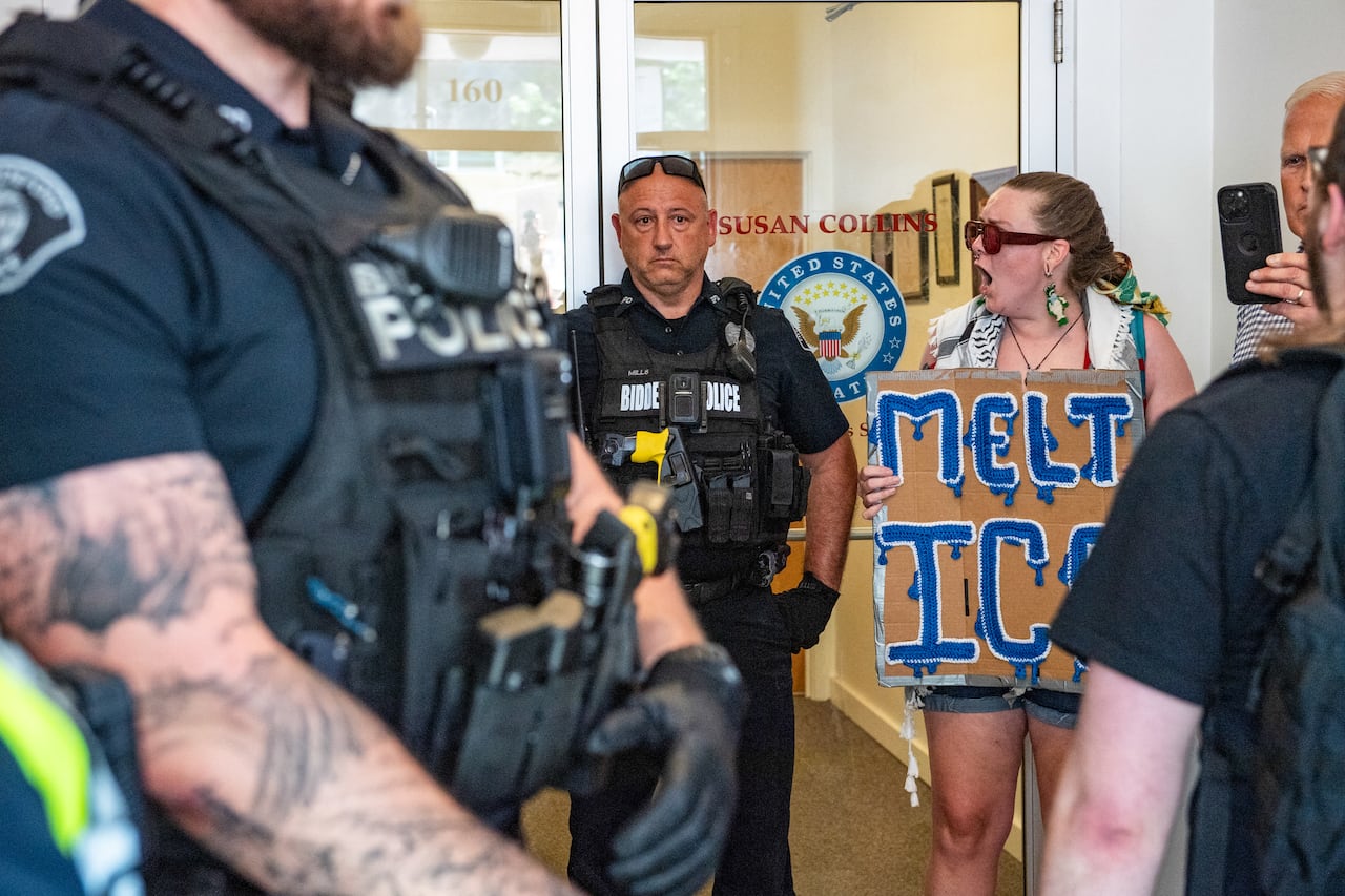 Police stand as people protest with signs.