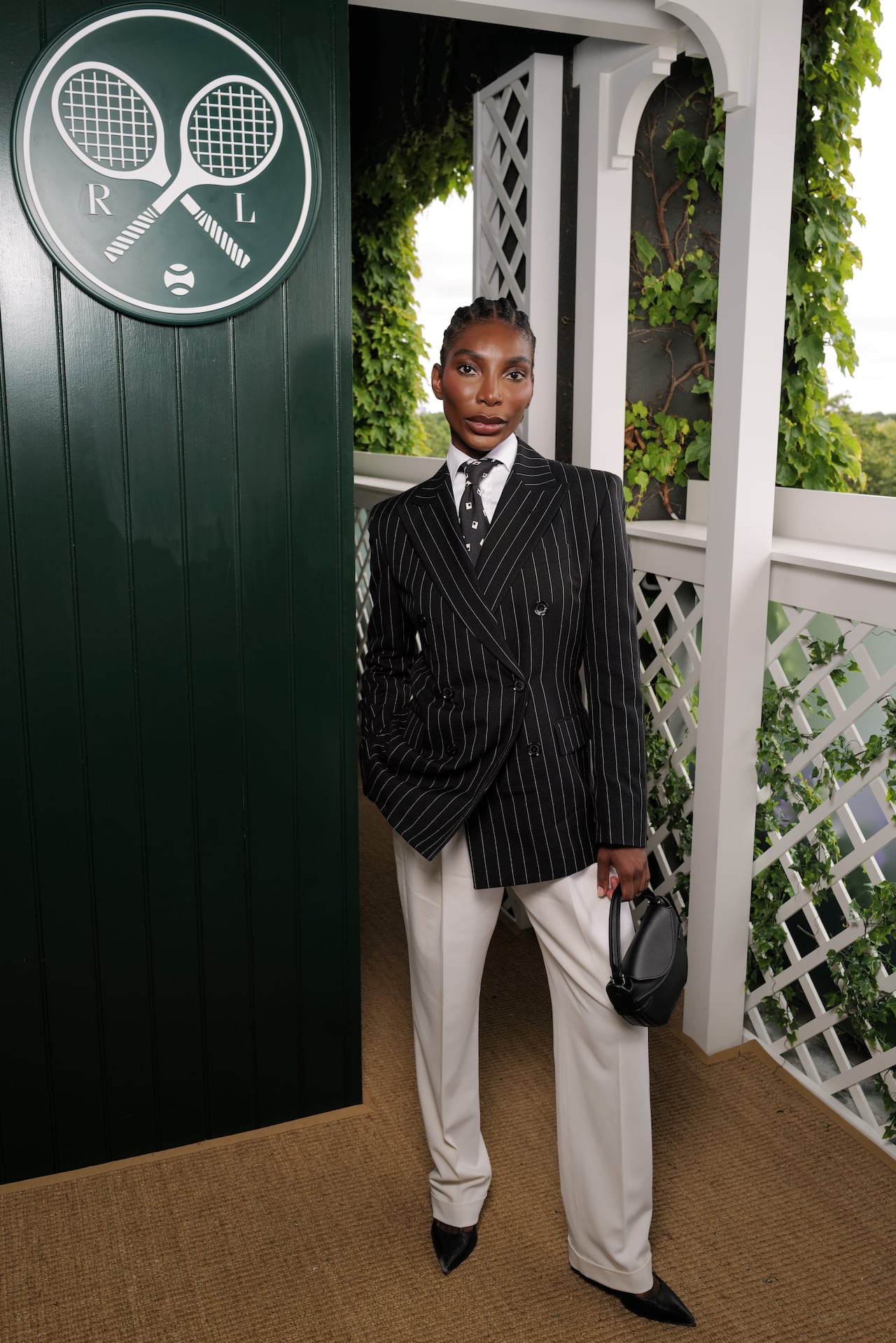 A woman poses for a photo wearing a black pinstripe suit jacket with beige trousers.