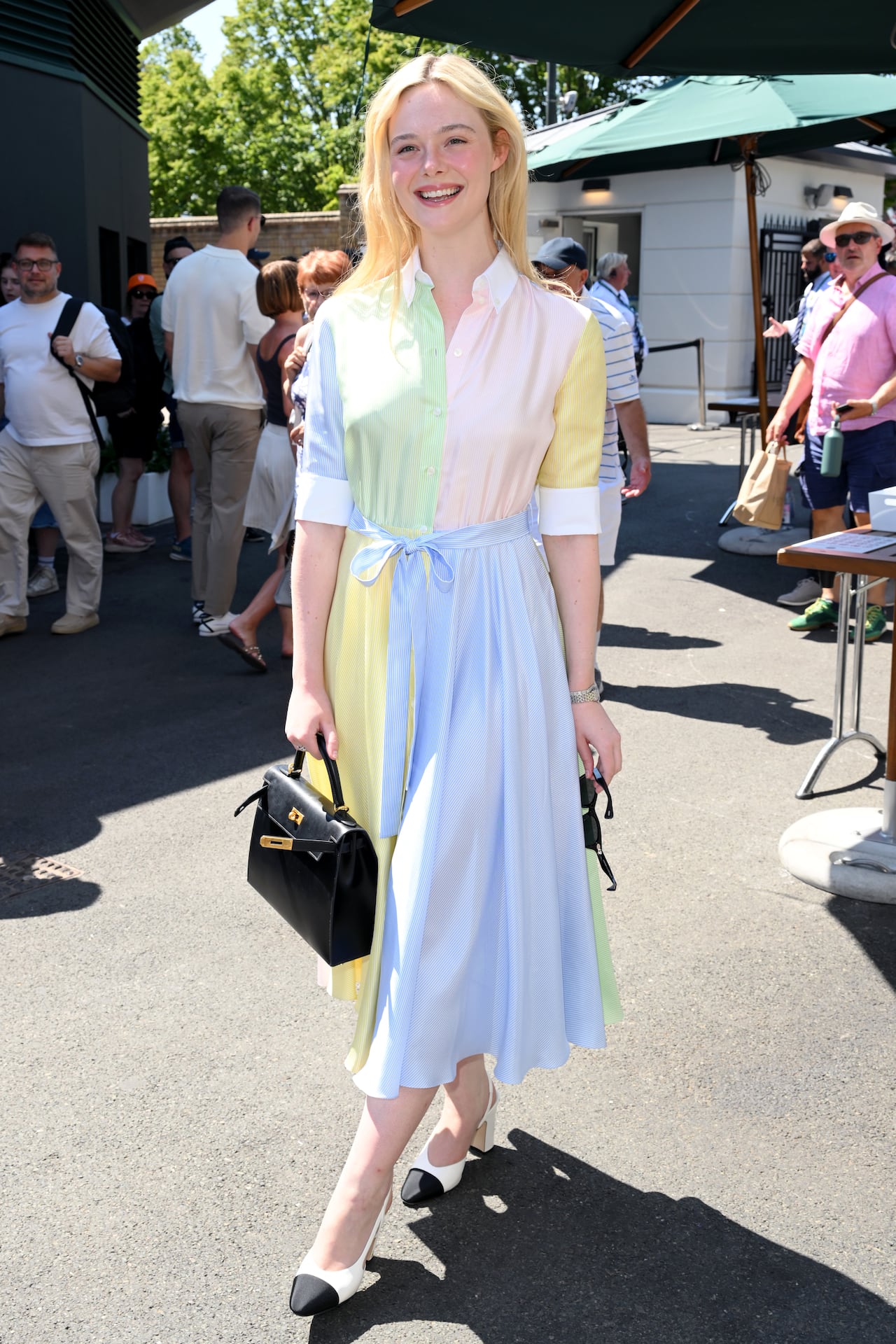 A woman poses for a photo wearing a colourful striped shirtdress, heels and carrying a purse.