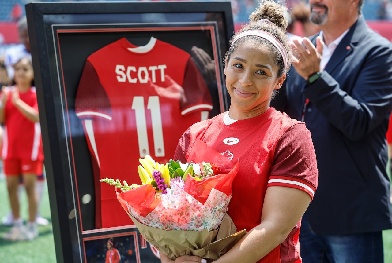 A women's soccer player smiles while holding a bouquet of flowers .