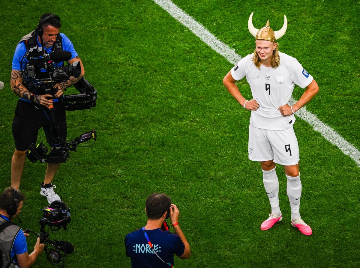 Erling Haaland wears a Viking helmet and a white uni as he poses on the pitch for photographers