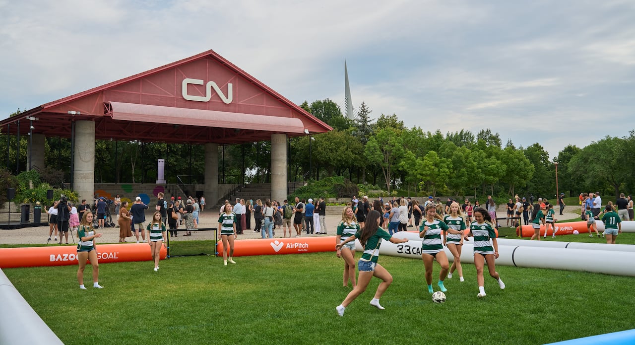 Girls in green and white jerseys play soccer in an area surrounded by inflated tubes.