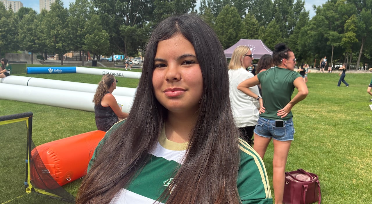 A girl in a green and white striped shirt looks at the camera.