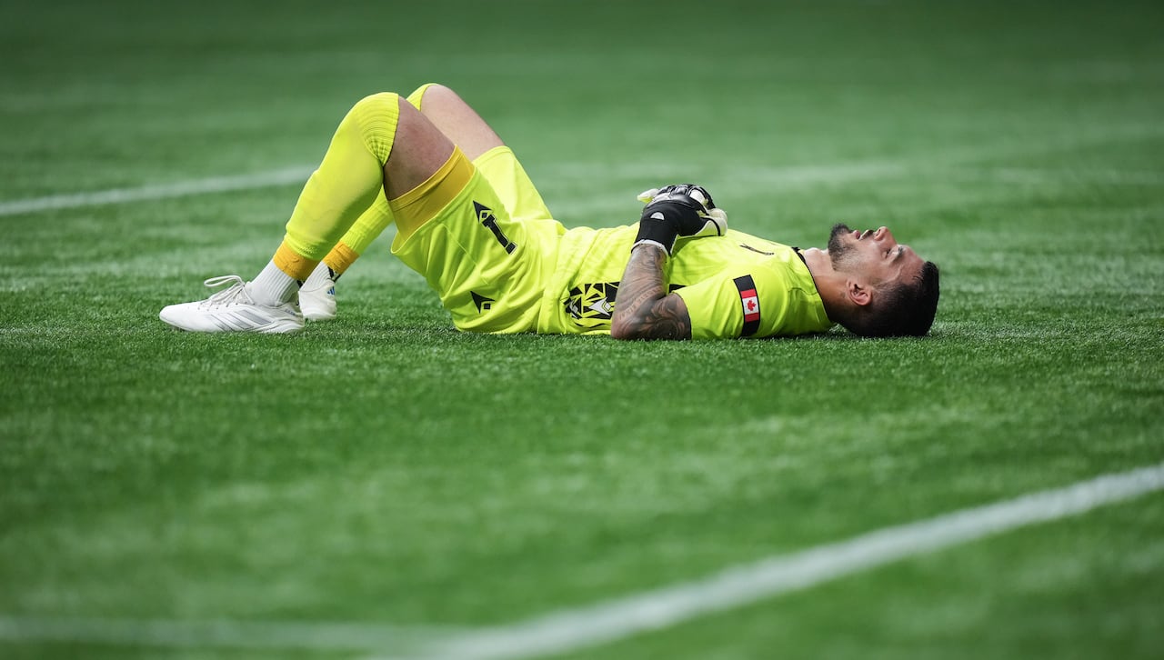 A man in a yellow soccer uniform lies on the turf of a playing field.