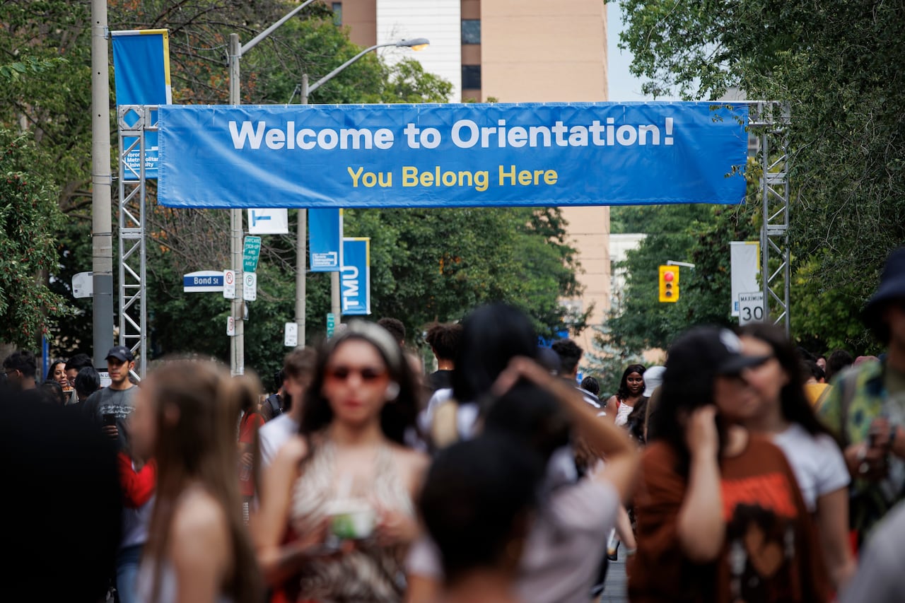 A large banner reading 'Welcome to Orientation! You Belong Here' is mounted outdoors over a pedestrian street, with students walking below it.