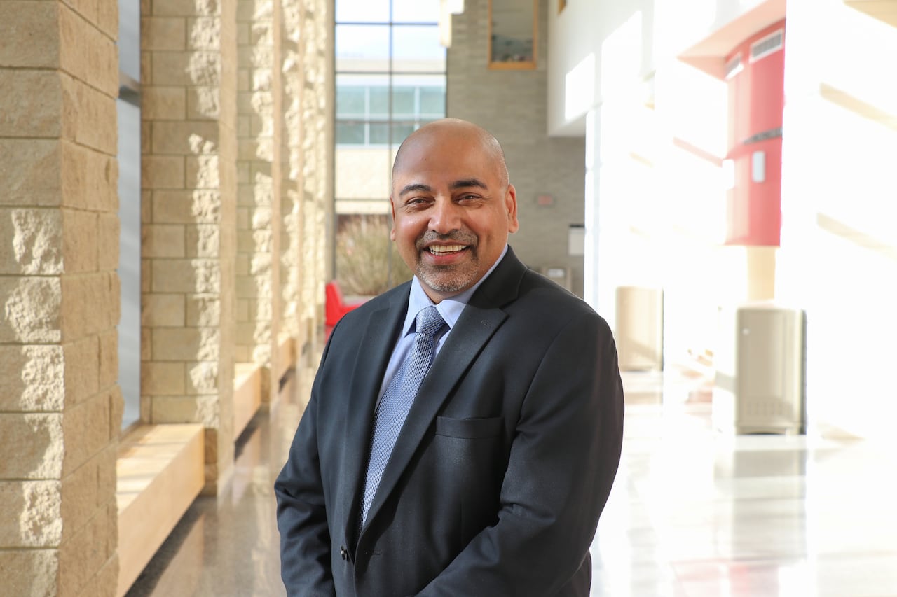A smiling man in a dark suit poses indoors in a bright atrium.