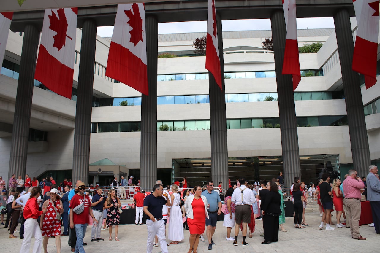 A crowd of people stand in a court yard with Canadian flags hanging above.