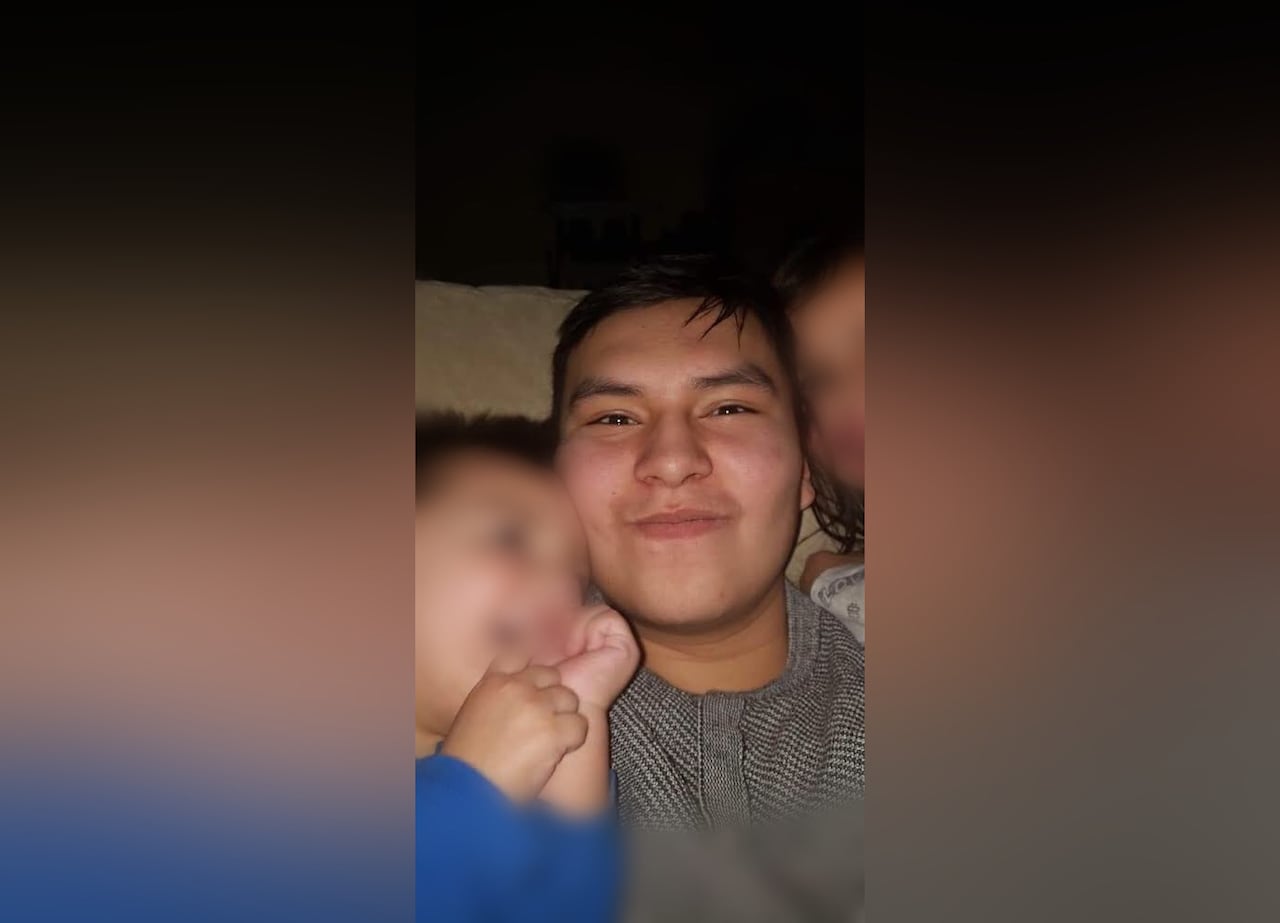A man is smiling to the camera, two children, with their faces blurred are besides him.
