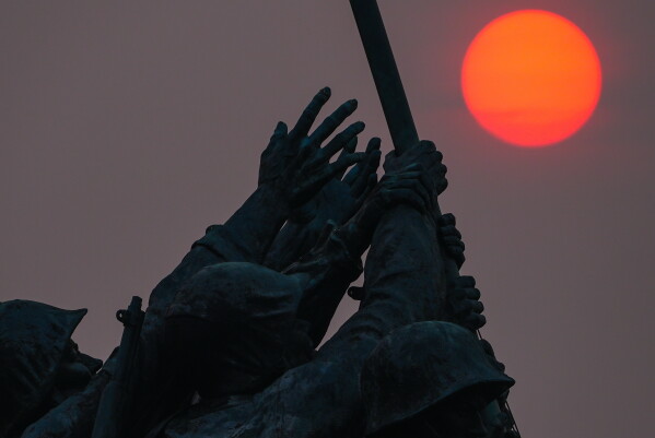 The sun is obscured by wildfire smoke as it rises behind the Marine Corps War Memorial, Friday, July 17, 2026, in Arlington, Va. (AP Photo/Julia Demaree Nikhinson)