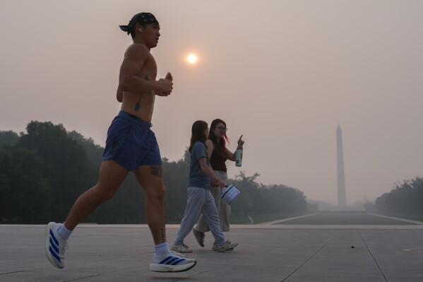 The sun is obscured by wildfire smoke as people run in front of the Washington Monument and Lincoln Memorial Reflecting Pool, Friday, July 17, 2026, on the National Mall in Washington. (AP Photo/Julia Demaree Nikhinson)